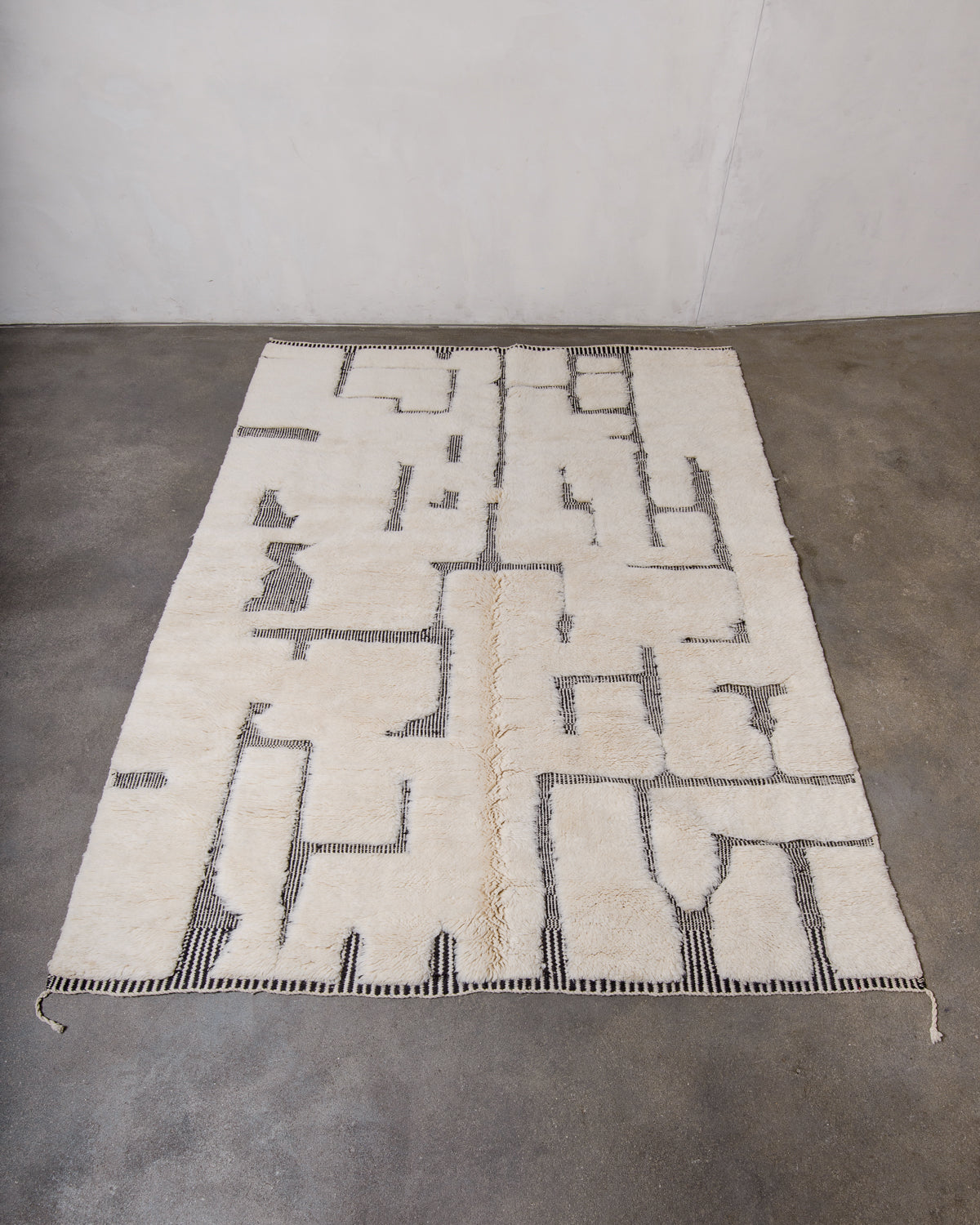 Beni M'rirt rug in cream wool with flat-woven design details in thin black and white stripes laying flat on concrete floor.